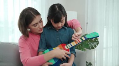 Kafkasyalı bir anne evde akustik müzik öğretirken ukulele çalan mutlu kız. Sevimli çocuk enstrüman öğreniyor. Kafkasyalı mutlu anne ve kız birlikte vakit geçiriyorlar. Pedagoji.