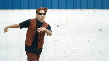 Beyaz arka planda break dans pratiği yapan yakışıklı bir sokak dansçısı. Hip hop tarzı giyinen sporcu, mavi arka planlı bir sokakta müzik eşliğinde ayak sesleri çıkarıyor. Açık hava sporu 2024 hiphop..