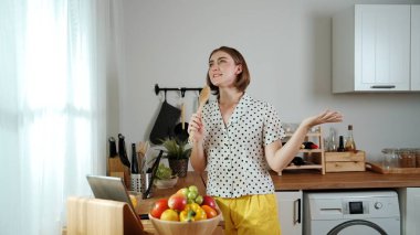 Kafkasyalı anne, modern mutfakta dizüstü bilgisayarda yemek tarifine bakarken salata yapmak için yemek hazırlıyor. Yetenekli ev bekçisi taze sebze kullanarak kahvaltı hazırlıyor. Pedagoji.