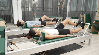 Vücut geliştirmek ve spor salonunda esnekliği arttırmak için çift pilates reformatörü üzerinde bacak egzersizi yapıyor. Pilates partneri bel kaslarını geliştirmek için pelvik köprü pozu veriyor. Alışkanlık.