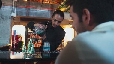 Barmen soğutma bardağına karışık mavi lagün kokteyli dökerken, misafirler içki bekleyen arkadaşlardan bahseder, çam ağacından yapılmış Noel temalı süslemeler özel şenlik tatlandırıcılarını çiftleştirir. Vinosity.