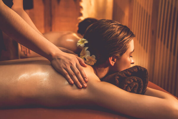 Caucasian couple customer enjoying relaxing anti-stress spa massage and pampering with beauty skin recreation leisure in warm candle lighting ambient salon spa at luxury resort or hotel. Quiescent