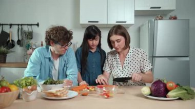 Çekici beyaz anne ve baba Asyalı kızıyla taze yemek pişirmek için birlikte vakit geçiriyorlar. Enerjik anne ve baba mutfakta salata yapmak için taze sebze hazırlıyor. Sağlıklı yiyecekler. Pedagoji.