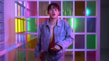 Kameraya bakarken kollarını esneten seksi kıyafetli Asyalı dansçı. Profesyonel sanatçı gece kulübünde renkli neon ışıkları canlı bir şekilde dururken serbest stil dansı yapıyor. Mutluluk.