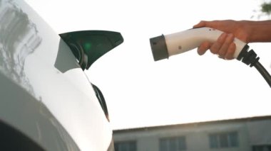 Genç adam, alışveriş merkezinin otoparkındaki EV otomobil şarj istasyonunda elektrik için akıllı telefon kullanıyor. EV aracıyla modern çevre ve sürdürülebilir kentsel yaşam tarzı