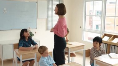 Sınıfta sınıf çalışmalarını anlatırken, sınıfta dolaşan beyaz bir öğretmen. Çekim eğitmeni konuşuyor ve çeşitli öğrenciler çalışırken ya da not alırken dersini anlatıyor. Eğitim. Pedagoji.