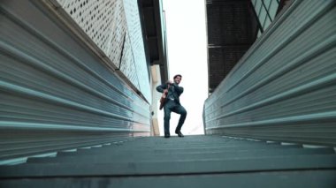 Genç gülümseyen iş adamının orta noktada dans edişinin düşük açılı görüntüsü. Takım elbise ve bavul giyip müziğe yönelen yetenekli bir yönetici. Müzikle ilgilenen mutlu yatırımcı. Sevinçli..