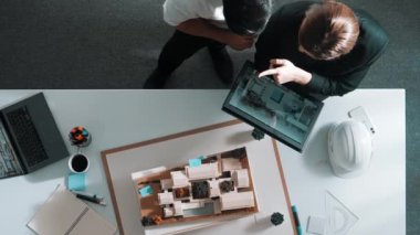 Tablet tutan akıllı yöneticinin yukarıdan görünüşü ve ev modeli ve mimari ekipmanlarla toplantı masasında dizüstü bilgisayar ekran binası inşaatına bakışı. Birlikte çalışan insanlar. Hizalama.
