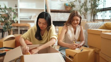 Çekici bir oda arkadaşı oturma odasında paket paketlerken pakette konum yazıyor. Mutlu satıcı birlikte çalışıyor ve teslimat paketini hazırlıyor. Girişimci kargo kutusu paketliyor. Myrmidon.