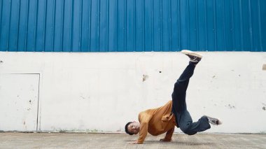 İspanyol adam kollarını açıp duvarın önünde dans ediyor. Modern dansçı ya da koreografın, günlük kıyafetleriyle hip hop stiliyle dans ederken ki hareketli çekimi. Açık hava sporu 2024. Hiphop.