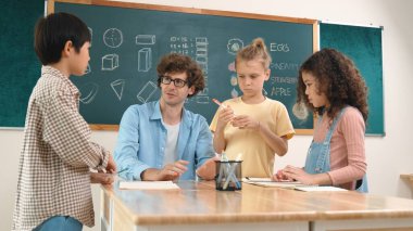 Zeki öğretmen, çeşitli çocuklar sınıf çalışması yapmak için birlikte çalışırken farklı çocukların zihin haritası çizdiği fikri açıklıyor. Çekici eğitmen öğretmek ve çalışmak hakkında konuşmak. Pedagoji.