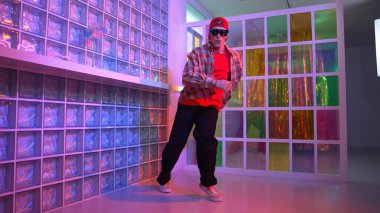 Komik break dansçı kameraya bakarken hiphop 'a doğru serbest adım atıyor. Çılgın mutlu hipster dans edip sokak dansı yaparken Led ışığında günlük kıyafet ve güneş gözlüğü takıyor. Mutluluk.