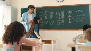Öğrenciye bakan beyaz bir öğretmen kendini karatahtaya tanıtıyor. Çeşitli öğrenciler karatahtaya bakarken sınıfın önünde duran çekici kız. Eğitim konsepti. Pedagoji.