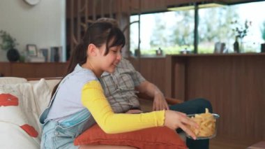 Grandfather and granddaughter eat french fries watch interesting entertainment on TV. Senior use technology communicate with young generation cross generation gap strengthen family bond. Divergence.