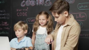 Çocuğun dizüstü bilgisayar mühendisliği kodunu ve yazım programını kullanırken bir grup zeki öğrencinin etrafı STEM teknoloji sınıfında arkadaşlarıyla çevriliyken karatahtaya oturması. Etkinlik.