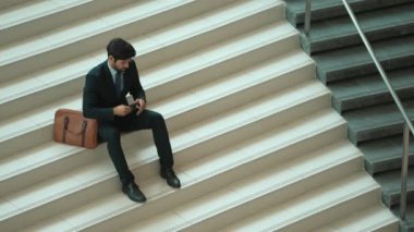 Akıllı bir iş adamının iş planı yapmak için telefon ve dizüstü bilgisayar kullanması. Merdivenlerde otururken. Müdür terfi alıyor, bilgisayarla arkadaşlarını ararken satışları arttırıyor. Sevinçli..