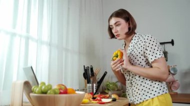 Kafkasyalı anne, modern mutfakta dizüstü bilgisayarda yemek tarifine bakarken salata yapmak için yemek hazırlıyor. Yetenekli ev bekçisi taze sebze kullanarak kahvaltı hazırlıyor. Pedagoji.