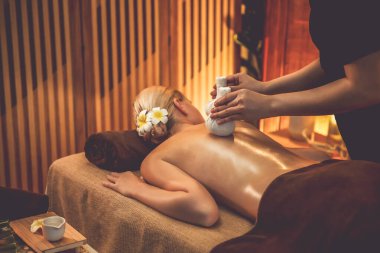 Sıcak bitkisel top spa masaj vücut tedavisi, masör kadın vücuduna nazikçe şifalı bitki torbası bastırıyor. Aromaterapi tesisinin sakinliği ve dinginliği kaplıca salonundaki mumların sıcacık ışığında. Sessiz.