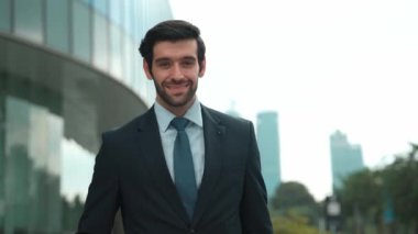 Profesyonel iş adamı hareket ediyor ve kameraya bakarken ayakta duruyor. Gülümseyen yönetici kameraya kendinden emin bir şekilde gülümsüyor. Mimari binada takım elbiseli yatırımcıların yakın çekimi. Sevinçli..