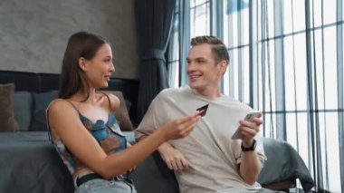 Genç çift, kredi kartıyla ödemek için internet üzerinden ödeme uygulaması ve dijital cüzdan kullanarak yatak odasında oturuyor. Mobil internet üzerinden alışveriş ve modern alımlar. Düzenle