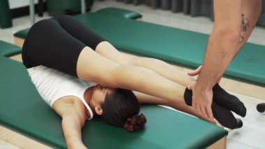Pilates müşterisi pilates minderinde yuvarlanırken bacak kaldırma alıştırması yapıyor. Kadın, karın bölgesini güçlendirmek ve esnekliği artırmak için antrenörlük yaparken ters duruşta poz veriyor. Alışkanlık.