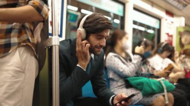 Gülümseyen yakışıklı yatırımcı trende otururken rahatlatıcı müzik dinliyor. Profesyonel iş adamı iş yerine toplu taşıma araçlarıyla giderken müzik dinlemeyi sever. Arka plan bulanık. Sevinçli..