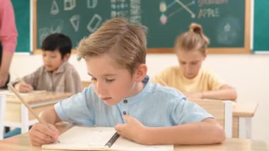Çekici beyaz çocuk okulda matematik okurken kameraya bakıyor. Çeşitli şirin öğrenciler test yaparken öğretmen Asyalı çocuklara soru sorup tahtaya kağıt doğrultuyor. Pedagoji.