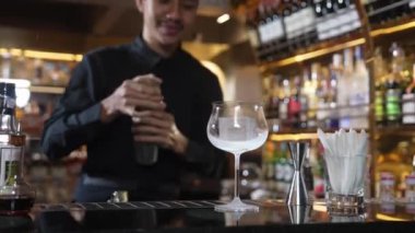Asyalı akıllı barmen karışık kokteyl sallayarak lüks tezgah hazırlıklarına hazırlanıyor, kameranın önüne bakarak özel bir içecek hazırlıyor. Özel gece hayatı lüksü. Vinosity.