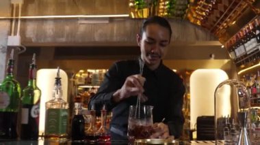 Zeki Asyalı barmen bardakta karıştırılmış alkol şurubunu buzla karıştırıyor. Çünkü kayanın üzerinde kamera var. Gece kulübünde taze kokteyl kokteylleri karıştırıyor. Vinosity.