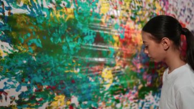 Genç mutlu kız renk tepsisini tutuyor ve fikri ifade etmek ve el iziyle hayal gücünü geliştirmek için renkli duvarları boyuyor. Resim dersinde odayı dekore etmek için beyaz kız pulu. Öğretim