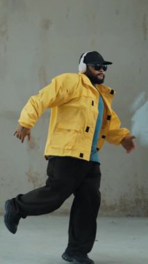 Hippi sokak, şehir merkezinde ayak izleri gösteriyor ya da pratik yapıyor. Break dansçının hareket halindeyken kulaklıktan müzik dinlediği sahne. Açık hava sporu 2024. Gri arka plan. Hip hop modası. hiphop.