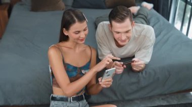 Genç çift, kredi kartıyla ödemek için internet üzerinden ödeme uygulaması ve dijital cüzdan kullanarak yatak odasında oturuyor. Mobil internet üzerinden alışveriş ve modern alımlar. Düzenle