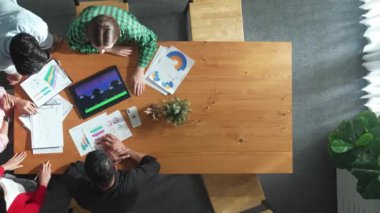 İş adamının tablet ekranını kullanmasına ilişkin en iyi bakış açısı artan grafiği kullanırken, farklı pazarlamacılar da fikir paylaşımı veya planlama stratejisini borsa istatistikleri etrafa saçılmış bir şekilde toplantı masasında paylaşıyorlar. Cemaat.