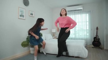 Yatak odasında Asyalı kızıyla müzik eşliğinde dans eden mutlu çekici anne. Beyaz anne dans eder ya da egzersiz yapar. Bu arada tatlı çocuk da müzik eşliğinde yatağa atlar. Aile eğlence konsepti. Pedagoji.