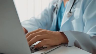Hastanedeki doktor masasında oturup dizüstü bilgisayar üzerinde çalışıyor. Hasta test sonuçlarını teşhis ediyor, hastalıklar ve hastalıklar için tedavi planı geliştiriyor. Sağlık personeli ve sağlık hizmetleri. Ağır çekim. Katı.