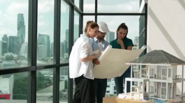 Profesyonel mimar mühendis ekibi konuşuyor, paylaşıyor, tasarım hakkında beyin fırtınası yapıyor. Yönetici planı dinlerken genç mimar plan yapıyor. İzleme