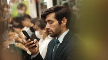 Gülümseyen beyaz iş adamı cep telefonuna bakıyor ya da trende otururken sosyal medya oynuyor. Çekici proje yöneticisi yoğun saatlerde toplu taşıma araçlarını kullanarak iş yerine gidiyor. Sevinçli..