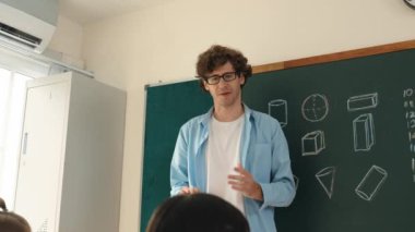 Zeki öğretmen sınıfta fikri açıklarken matematik teorisine işaret ediyor. Profesyonel eğitmen, öğrenciye bakıp matematik dersinde tahtaya basarak fikir hakkında konuşuyor. Pedagoji.