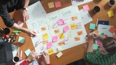 Akıllı iş adamlarının toplantı odasında kargaşa çıkaran görev panolarının yukarıdan görünüşü. Kanban tahtası yapıp beşlik çaktıkları için kağıt ve yapışkan notlar yazan bir grup zeki insan. Cemaat.