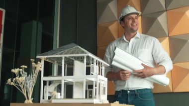 Masada ev modeliyle proje planı tutan Kafkas profesyonel proje yöneticisi. Kendine güvenen bir şekilde poz verirken güvenlik kaskı takan profesyonel mimar mühendisi. Yönlendirici.
