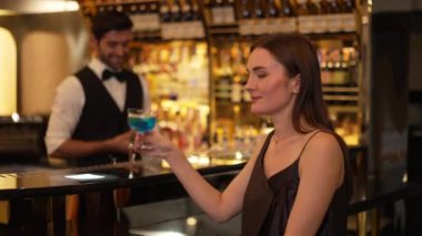 Güzel bayan konuk kameraya bakarak poz veriyor. Kulüpteki akıllı barmen geçmişi ile ilgili toplantı için lüks tezgah barında mavi Hawaii kokteyli ile karışık votka içiyor. Vinosity.