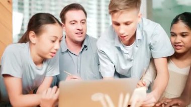 Beyaz bir öğretmen, genç bir öğrenciye nasihat verirken, bir çocuk da ders veriyor. Profesyonel eğitmen, masada dizüstü bilgisayarı ve kağıdı olan çok kültürlü çocuklarla çevrili yorumlar yazar. Öğretim