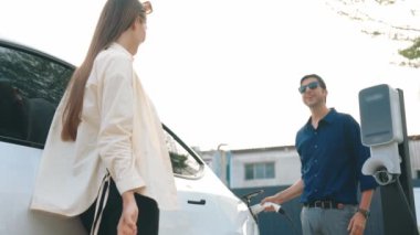 Yavaş çekim çift, alışveriş merkezinin otoparkındaki şarj istasyonundan elektrikli araba aküsünü şarj ediyor. Enerji sürdürülebilir kentsel seyahat yaşam tarzı için şarj edilebilir EV araba