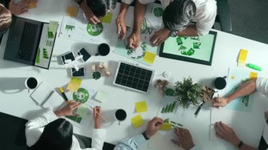 İş adamlarının rüzgar değirmeniyle toplantı masasında temiz enerji ve sürdürülebilir yatırım kullanımı, çevre grafiği ve ahşap ev modeli ile ilgili tartışmalarına tepeden aşağı bakış açısı. Hizalama.