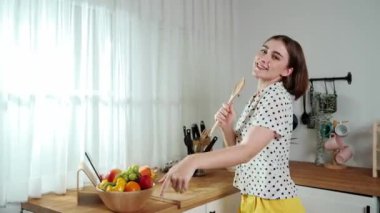 Enerjik beyaz anne kahvaltı için salata pişirirken ve yemek pişirirken elinde kepçeyle şarkı söylüyor. Sağlıklı yemek yapmaya hazırlanırken müziğe yönelen mutlu ev sahibi. Pedagoji.