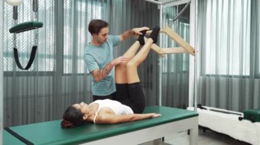 Pilates hocası, Cadillac teçhizatı üzerindeki bacak kaldırma egzersizi sırasında bir müşteriye yardım ediyor. Öğrenci uzanıyor ve temel dayanıklılık ve bacak esnekliğini arttırmak için Cadillac 'ın üzerinde bacak daire çiziyor. Alışkanlık.