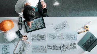 Bina yapısını analiz etmek için dizüstü bilgisayar kullanırken tablete bakan mühendislerin yukarıdan aşağı görüntüsü. Proje planıyla toplantı masasında iç tasarımı kontrol eden mimarın hava görüntüsü. Hizalama.