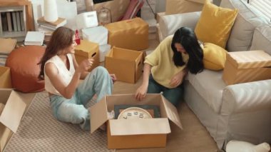 Lezbiyen aşıklar taşınma gününde karton kutudan nesneleri alıyorlar. Taşınırken paketleri açmak ve kutudan mobilya toplamak için birlikte çalışan bir çift oda arkadaşı. Yer değiştirme konsepti. Myrmidon.