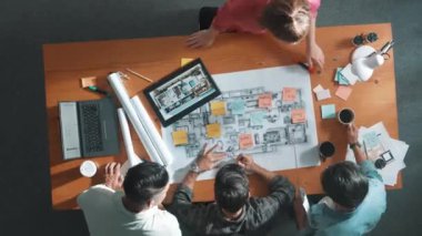 İnşaat mühendisi ekibinin toplantı odasında çalışmaya hazırlanması zaman aşımı. Akıllı mimarın bina inşaatı sırasında masa ve yer proje planında yürüdüğünü en tepeden aşağıya gösteren hava manzarası. Sempozyum.