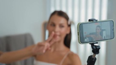 Genç sosyal medyum kadın moda videosu yapıyor. Blogcu kameraya selfie çubuğu ve ışık halkası kullanarak gülümserken, aynı zamanda ikna edici çevrimiçi kıyafetlerin izleyicilere veya takipçilere vlog satmasını sağlıyor. Düzenle